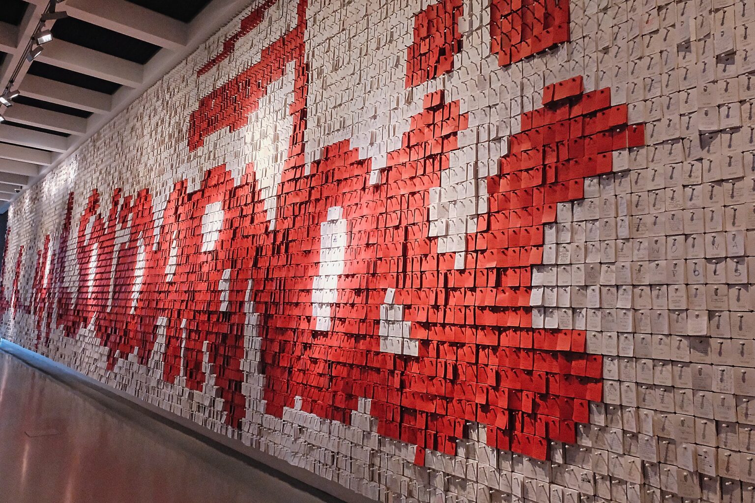 Interior perspective of a commemorative wall covered in thousands of small red and white notes forming a graphic display at the European Solidarity Centre.