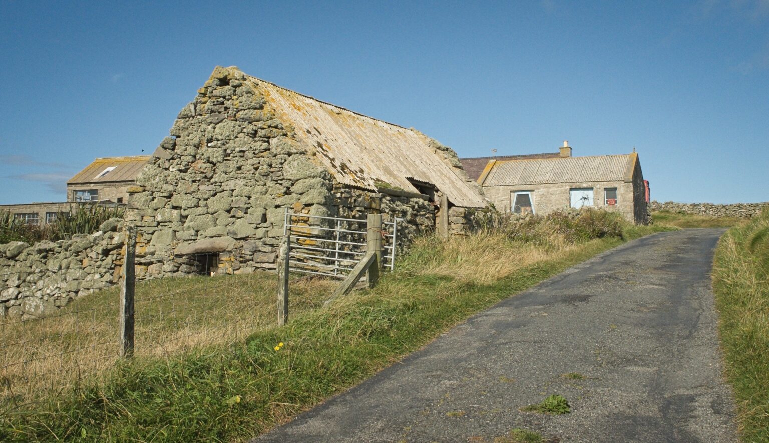 A minimalist architectural shot of a preserved stone croft building with a corrugated roof, standing against the rugged horizon