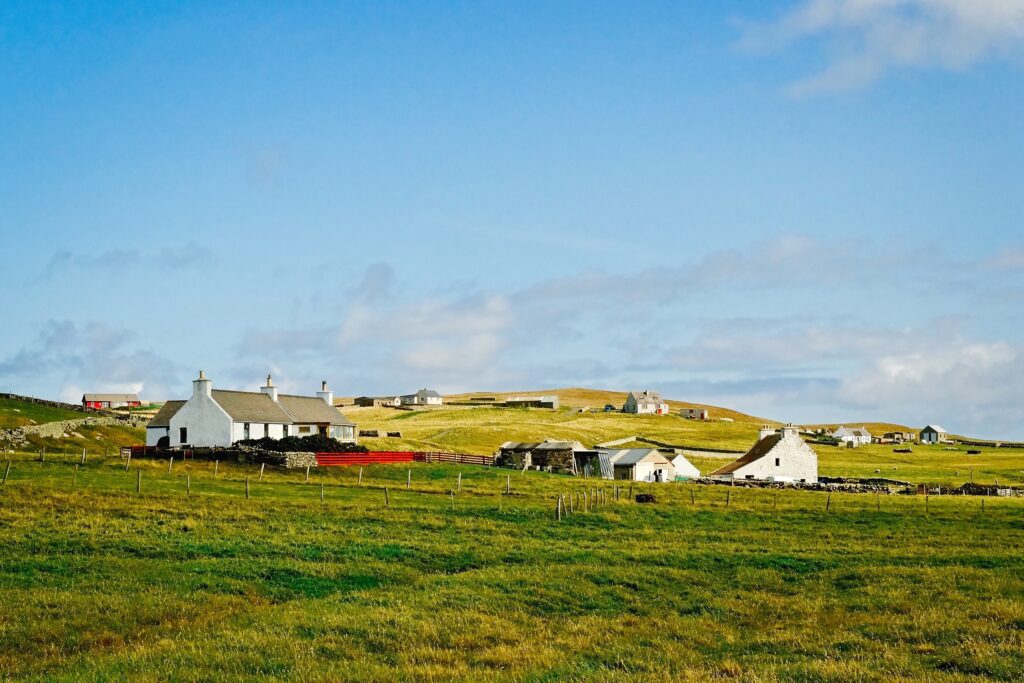 Expansive landscape shot of traditional white houses scattered across the vibrant green hills of Fair Isle
