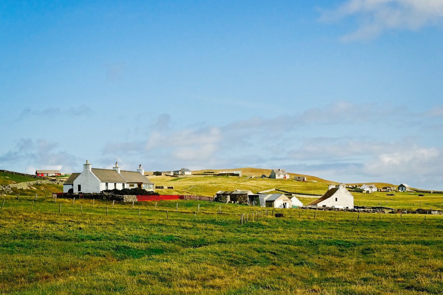 Expansive landscape shot of traditional white houses scattered across the vibrant green hills of Fair Isle