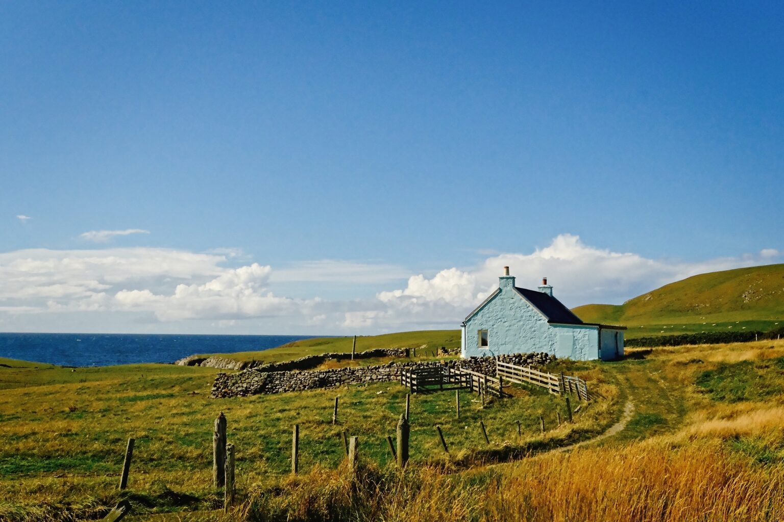 Cinematic landscape photography of a lone white cottage nestled in the rugged green hills of Fair Isle, Scotland.