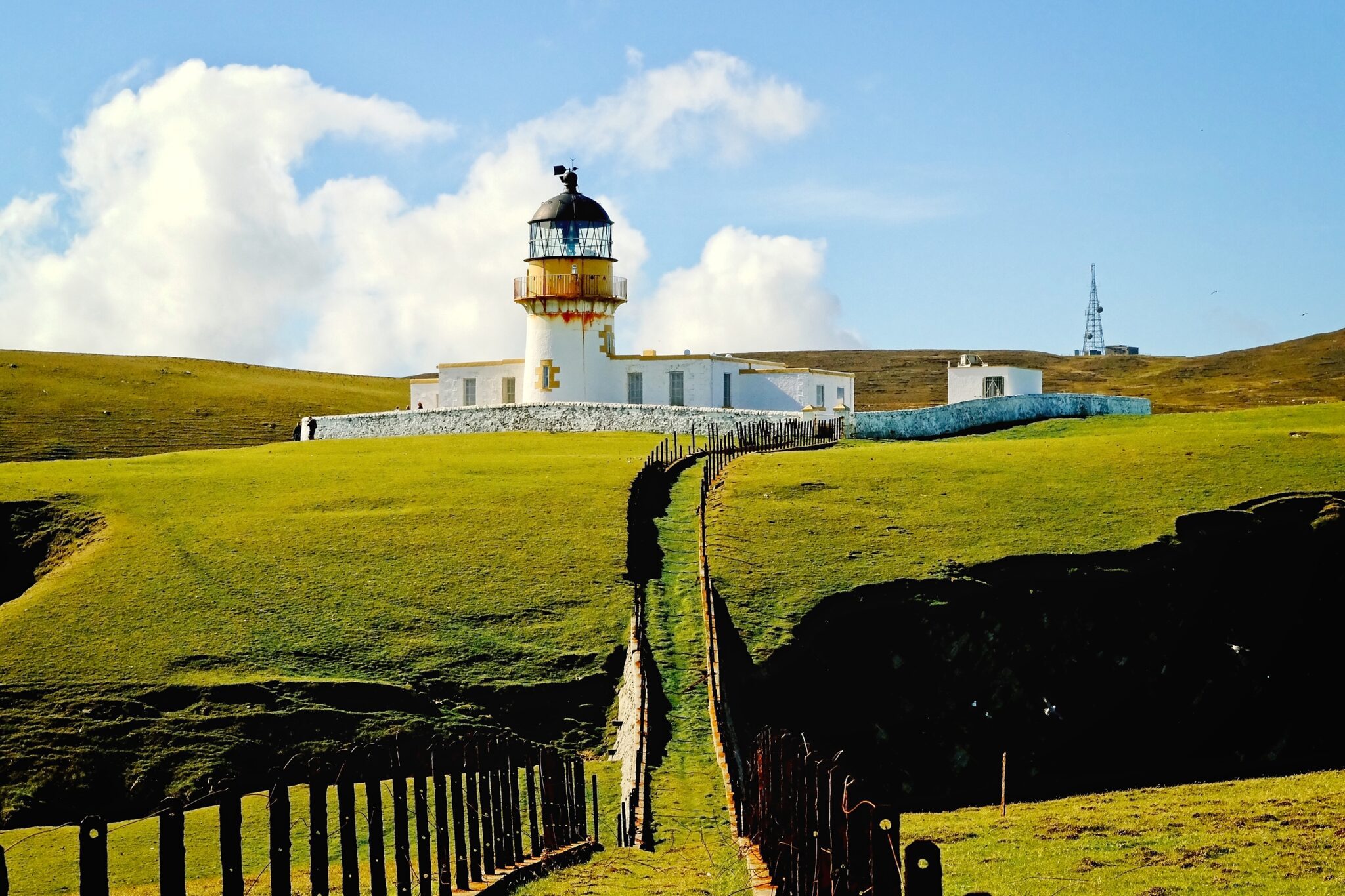 Cinematic wide-angle photography of a Fair Isle lighthouse standing sentinel on a dramatic green cliffside under a soft Scottish sky