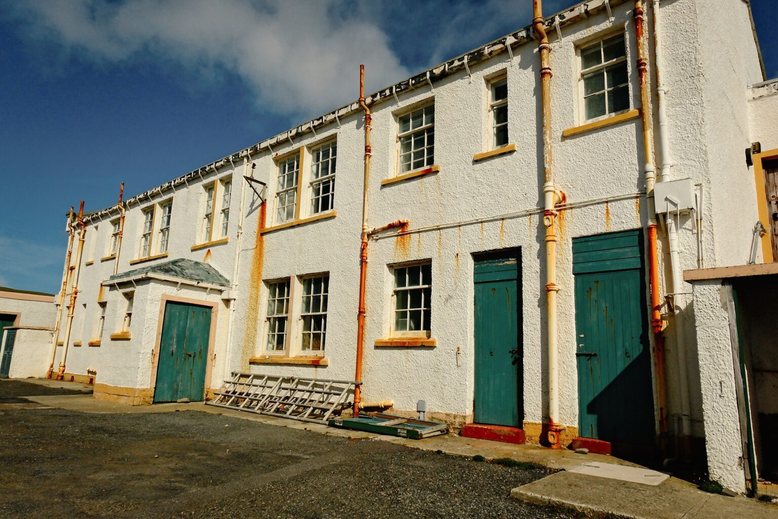 A wide architectural study of the white-washed light house buildings with a weathered drainpipes