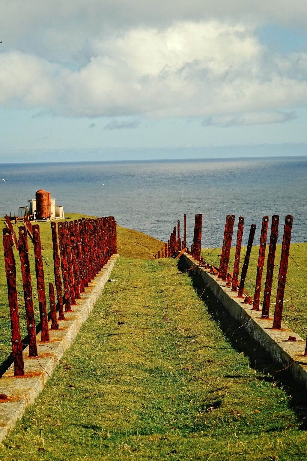 Leading lines of a weathered red metal fence guiding the eye through to a coastal warning station