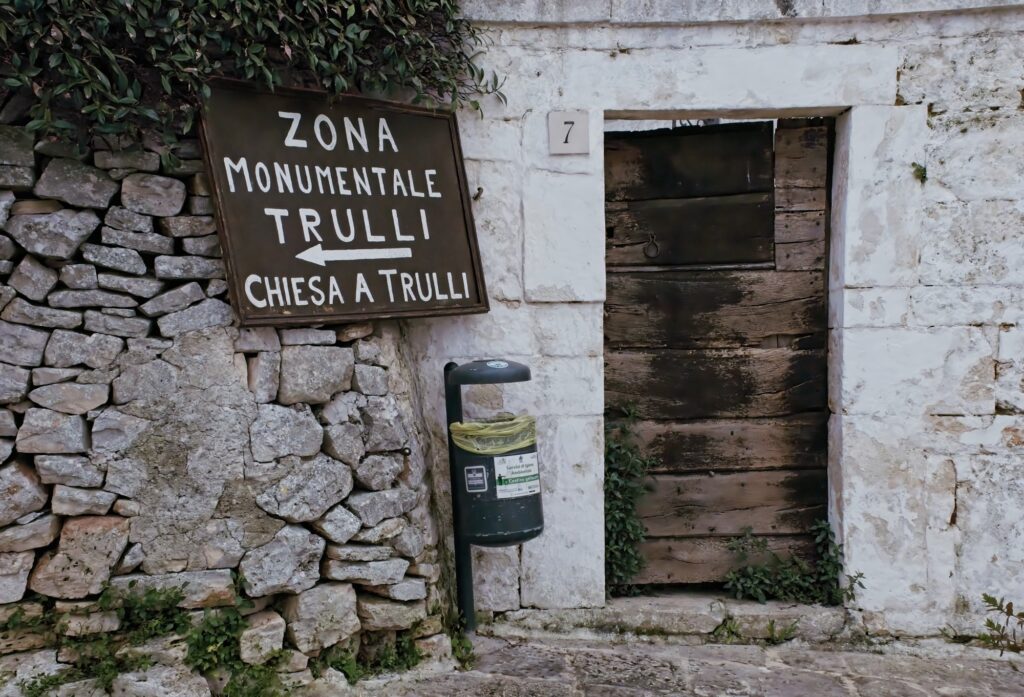 Close-up architectural detail of a weathered stone sign for the 'Zona Monumentale Trulli' in Alberobello