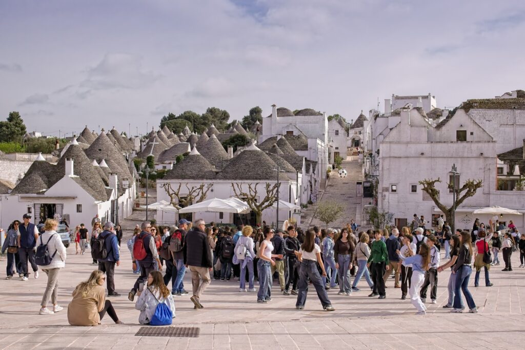 Documentary photography of a bustling crowd in the historic center of Alberobello, showcasing the unique conical Trulli roofs