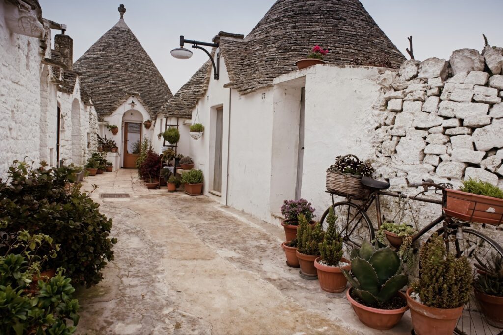 A quiet, trulli side street in Alberobello featuring white-washed walls and blooming flower pots