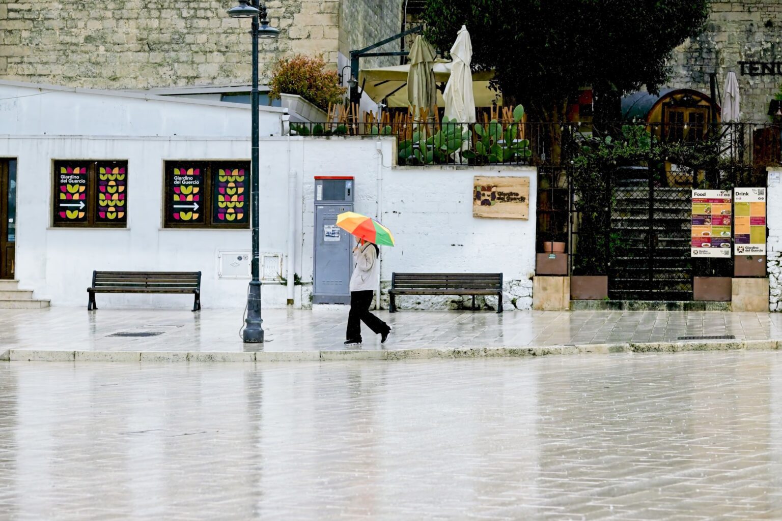 Observational wide shot of a tourist navigating a sudden rain shower in a traditional Puglia street