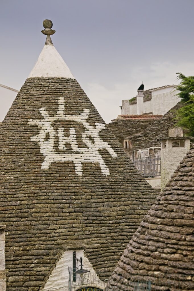 Architectural editorial shot of a white religious symbol painted on a traditional limestone Trullo roof