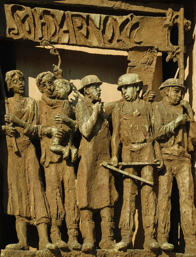 A bronze bas-relief sculpture titled "Solidarność" (Solidarity), depicting a group of shipyard workers, a woman, and a man holding a child, symbolizing the collective unity of the Polish labor movement.