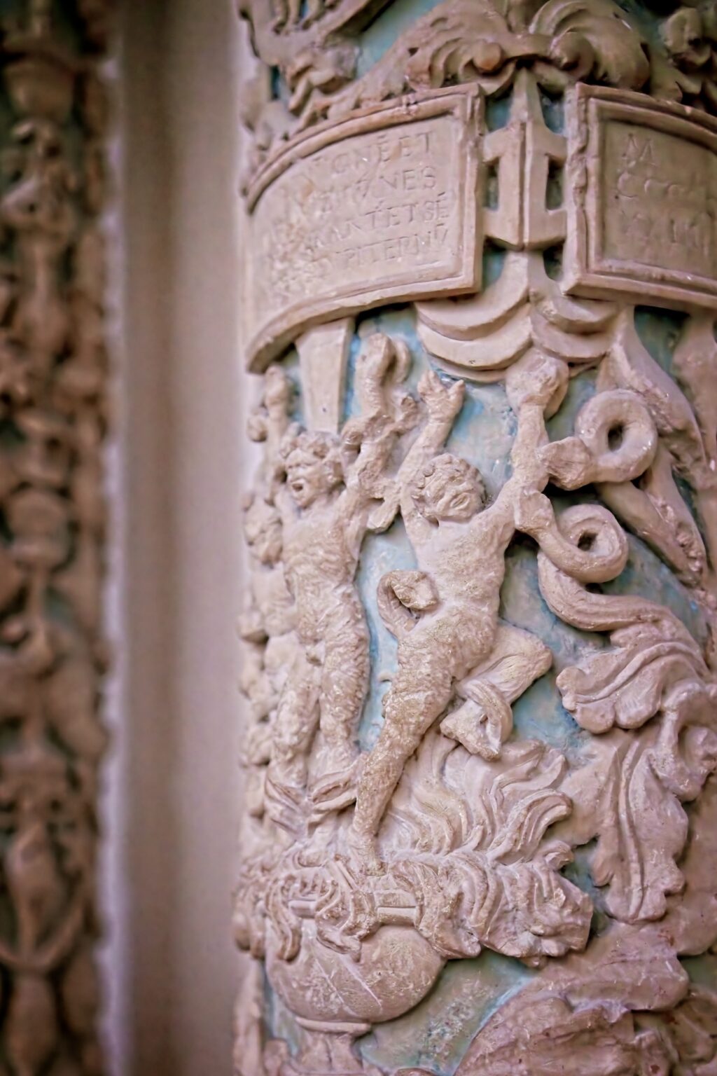 Detailed architectural photography focusing on intricate stone carvings of figures and Latin inscriptions on a historic cathedral column, captured with a shallow depth of field