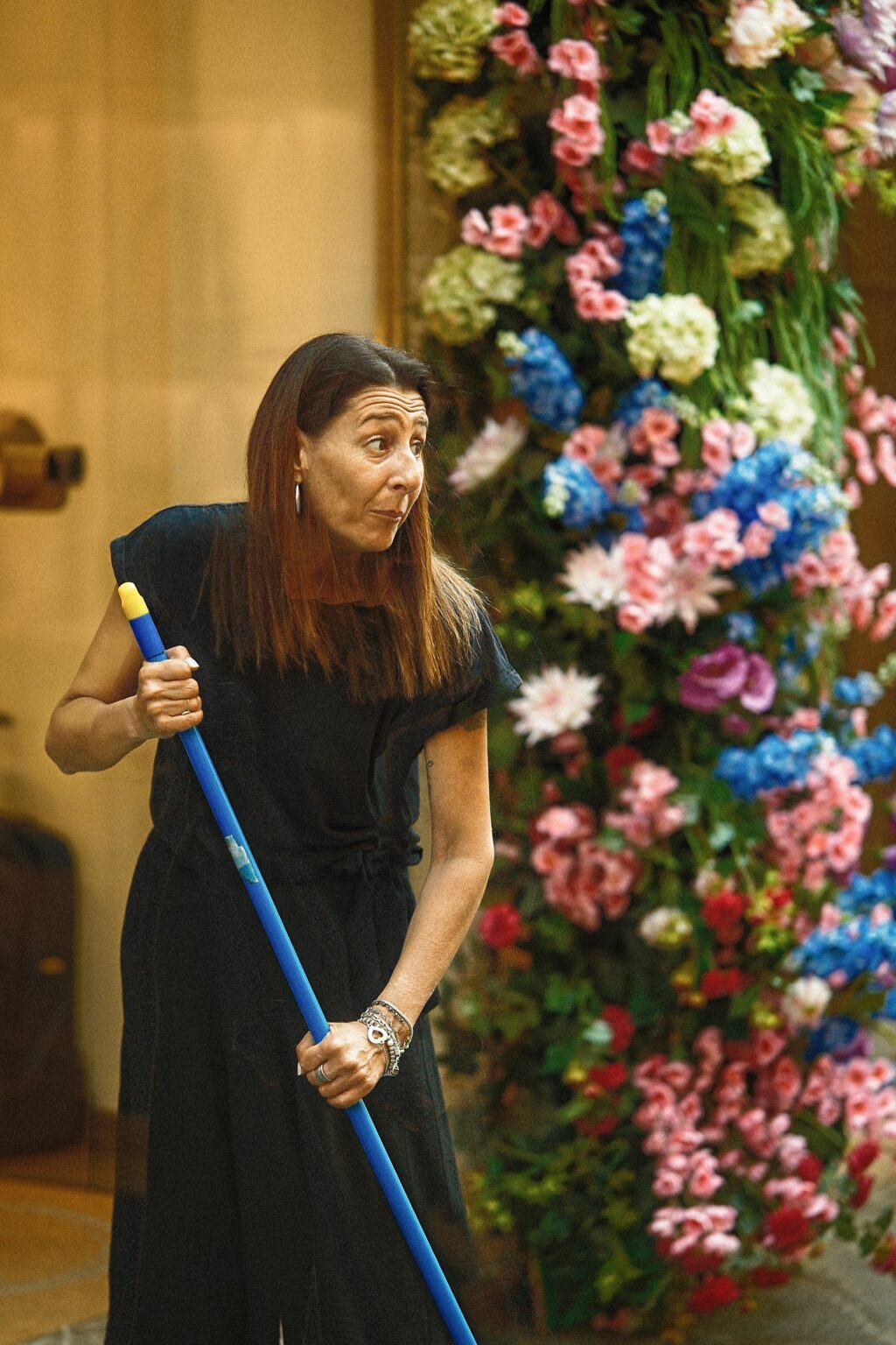 Candid editorial shot of a woman sweeping the entrance of a shop surrounded by cascading floral displays