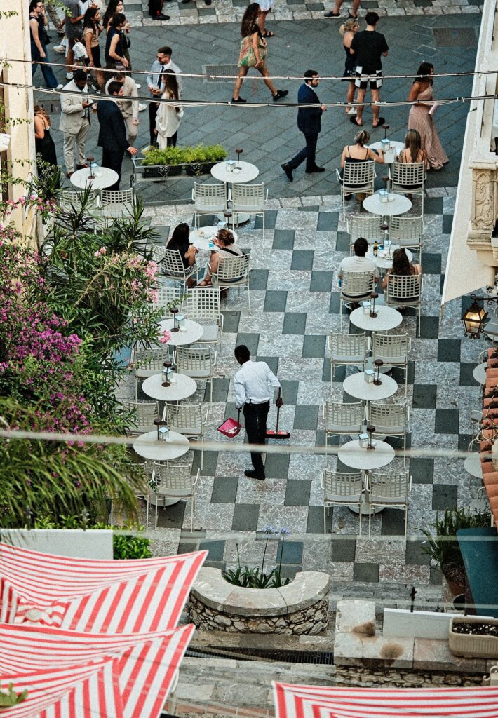 High-angle perspective of a monochrome tiled piazza with figures walking through long shadows in Taormina