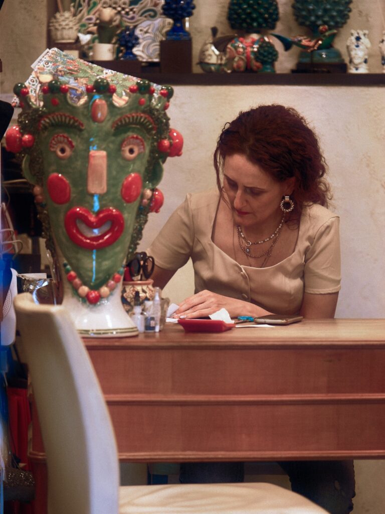 Observational moment of a woman working behind a desk surrounded by colorful Sicilian ceramics