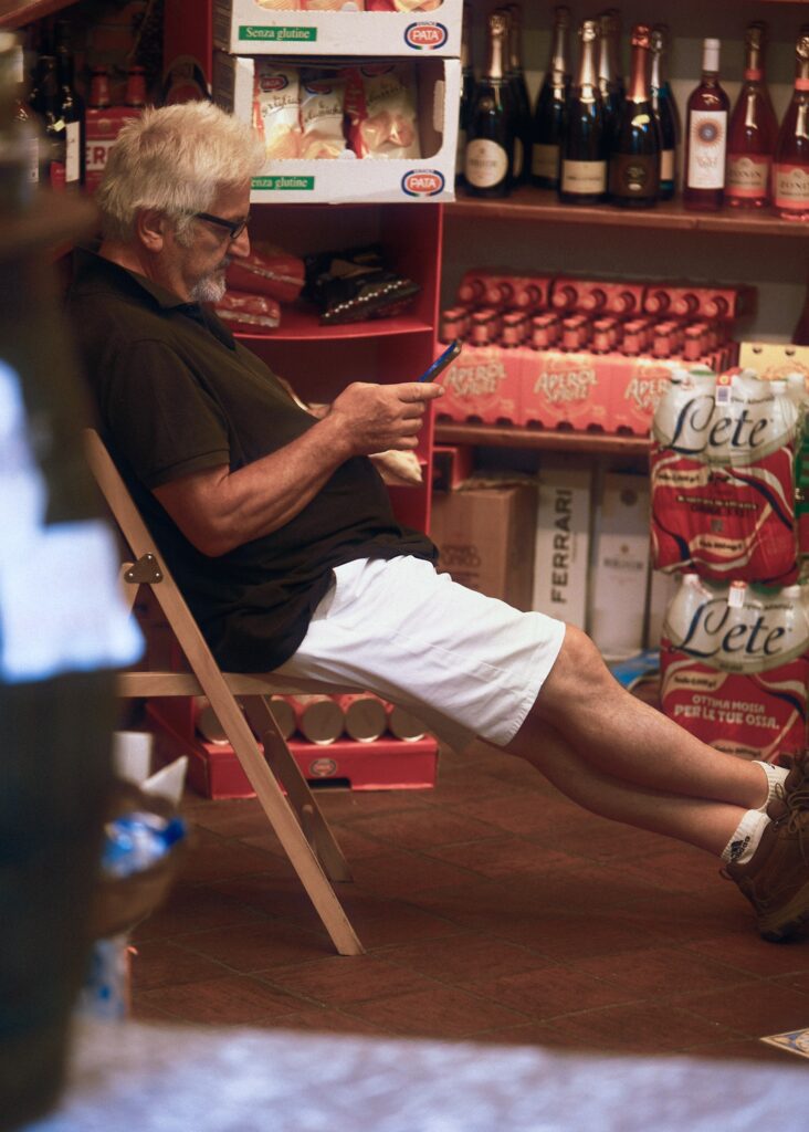 A quiet documentary moment of a person sitting in the doorway of a local boutique in Taormina.