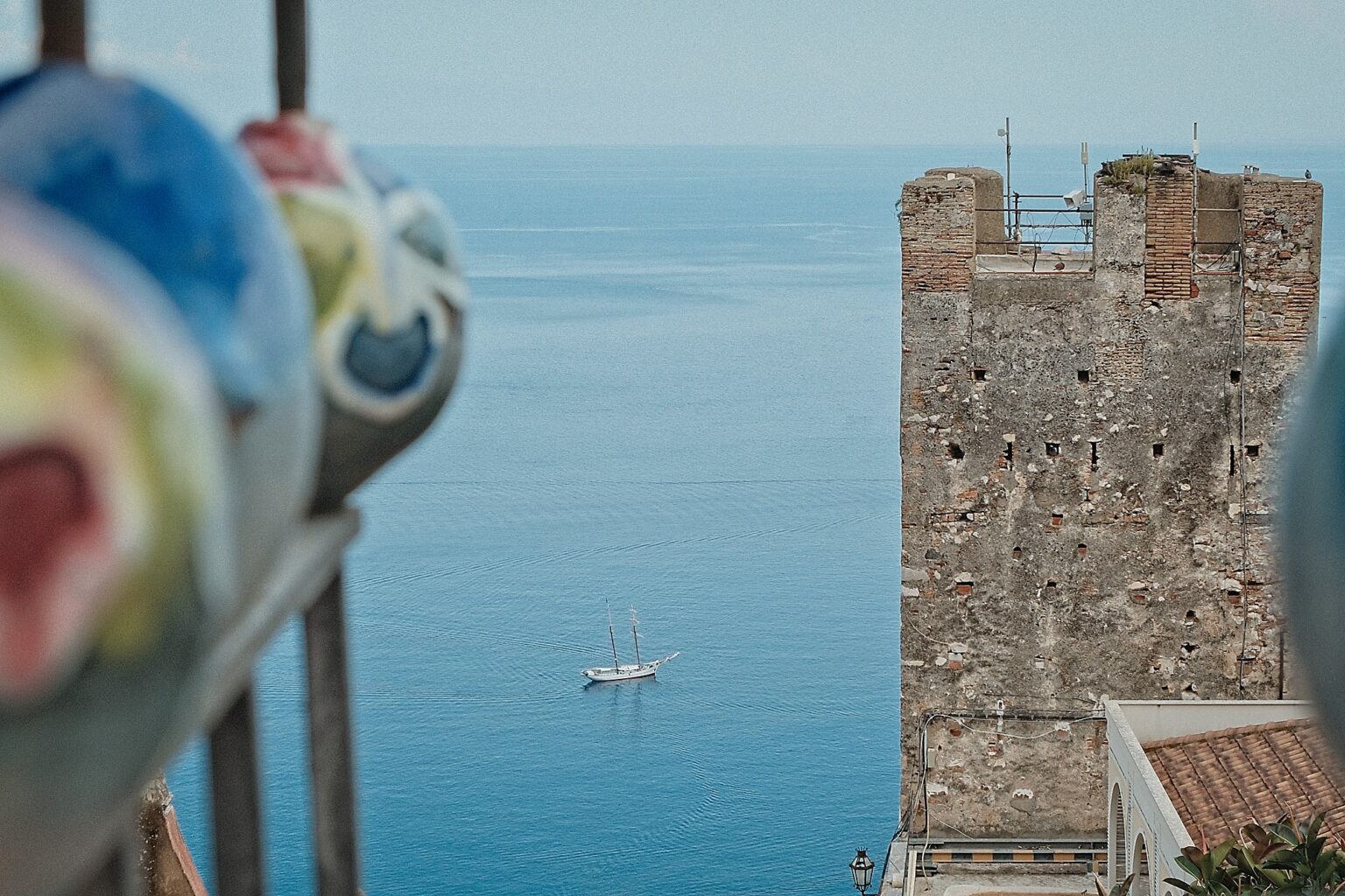 Minimalist landscape photography of an ancient stone tower overlooking the blue Ionian Sea with yacht in distance
