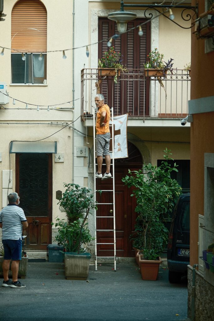 Observational street scene of a person on a ladder working on a traditional white-washed facade.