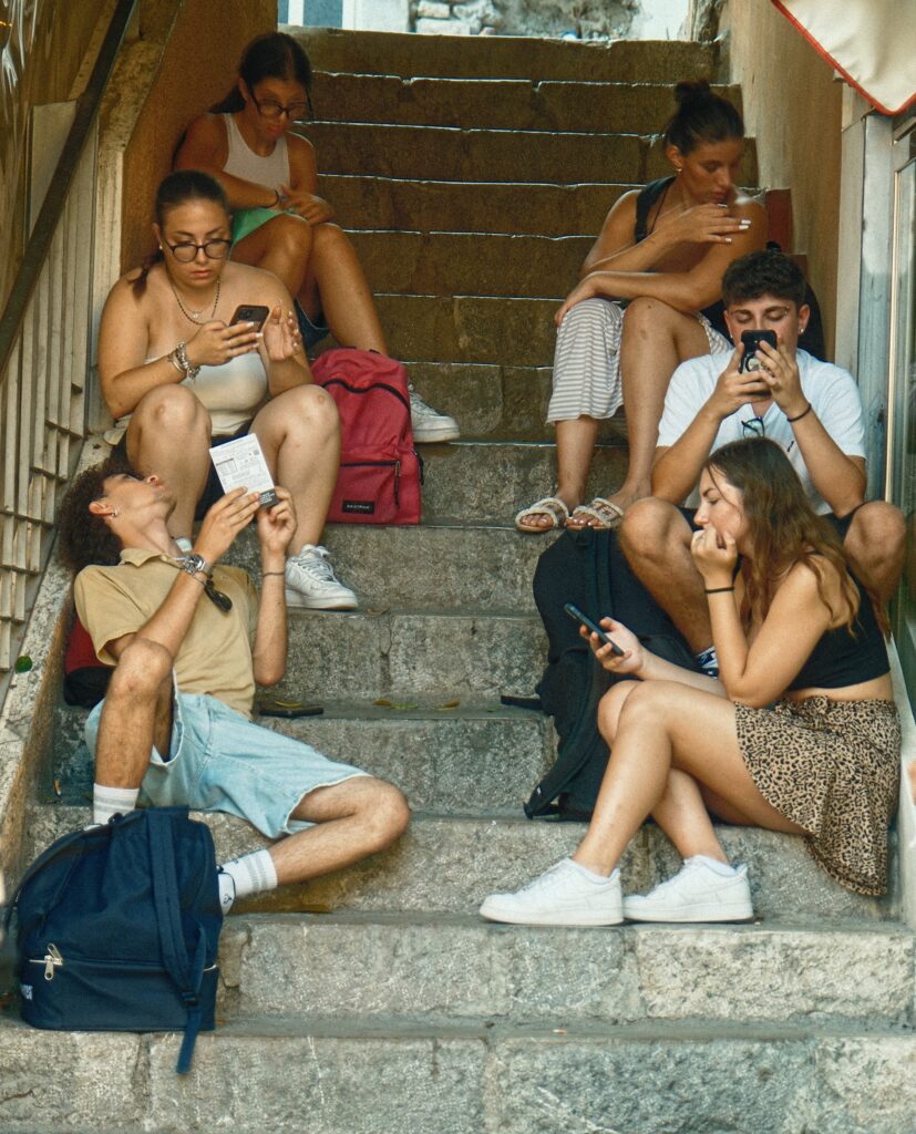 Grounded documentary photography of a group of young people sitting and talking on the ancient stone steps of Taormina