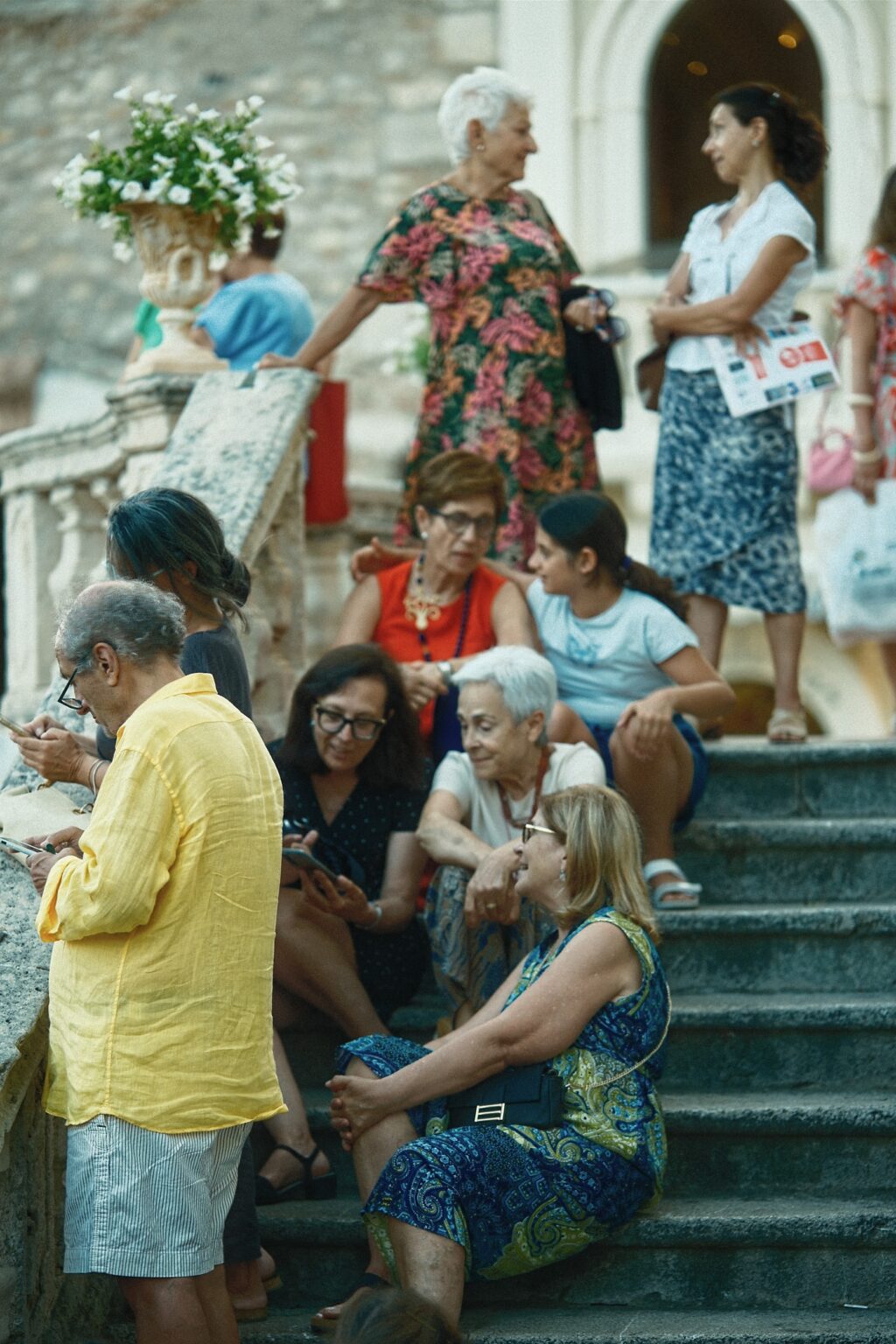 Candid documentary moment of groups of friends gathered on the stone steps of a Taormina church