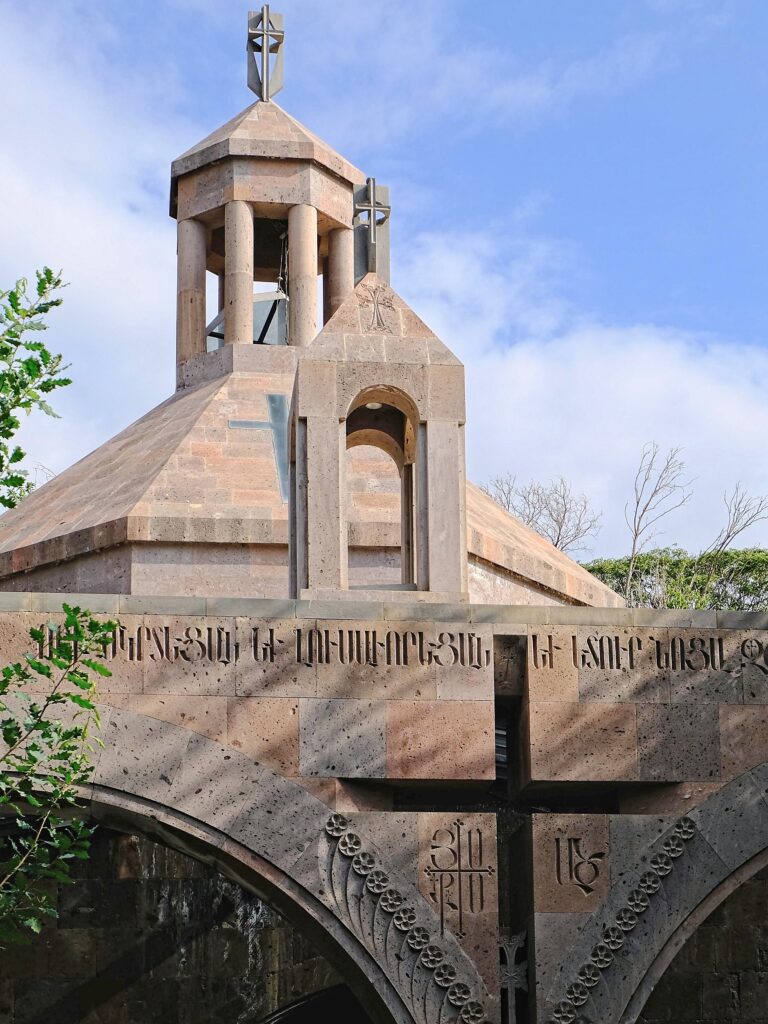 A quiet, architectural study of a modern orthodox stone belfry with a silhouetted cross in the foreground