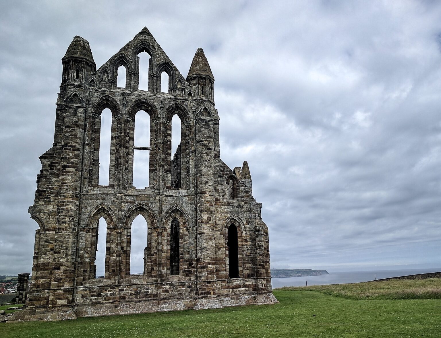 Atmospheric landscape shot of the skeletal stone remains of Whitby abbey against a moody, overcast sky.
