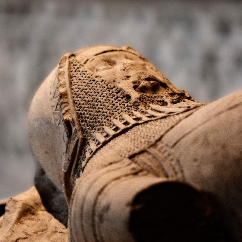 A close-up, shallow depth-of-field texture study of a carved stone medieval figure on a tomb