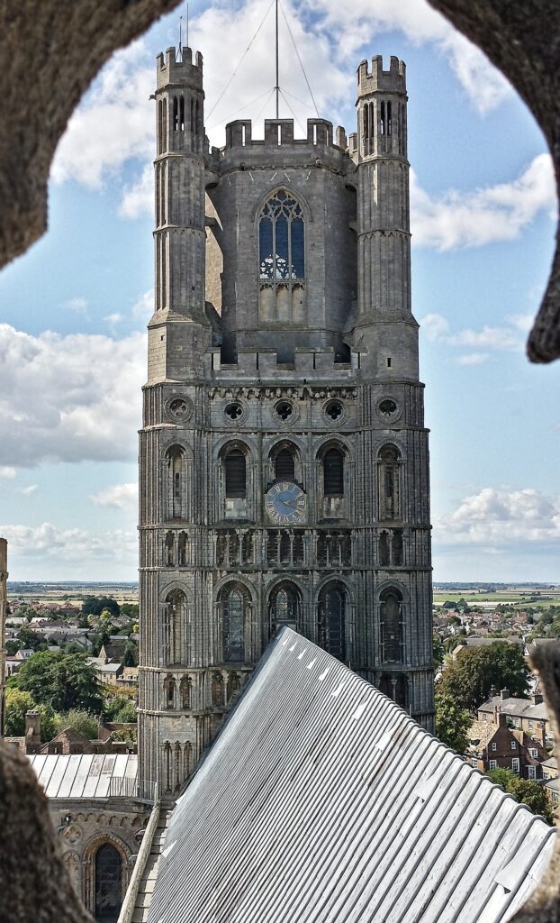 Low-angle architectural editorial of the massive stone Ely cathedral tower under a bright, clear sky.