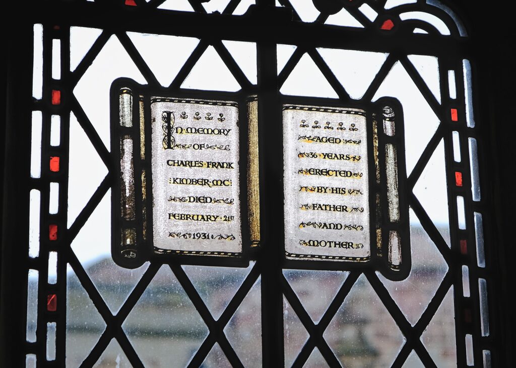 A high-contrast observational shot of text of rememberance seen through a dark, leaded glass window