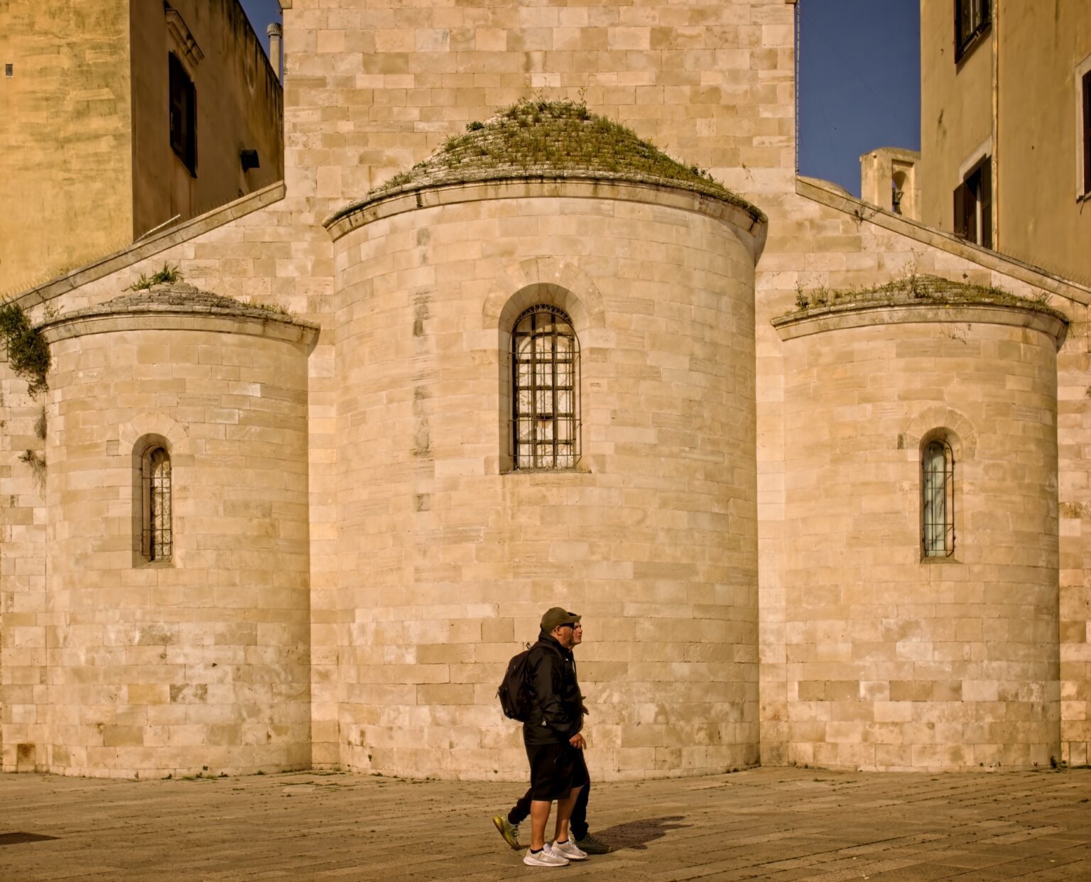 Cinematic street photography of a two figures walking past the ancient limestone walls of a Bari church