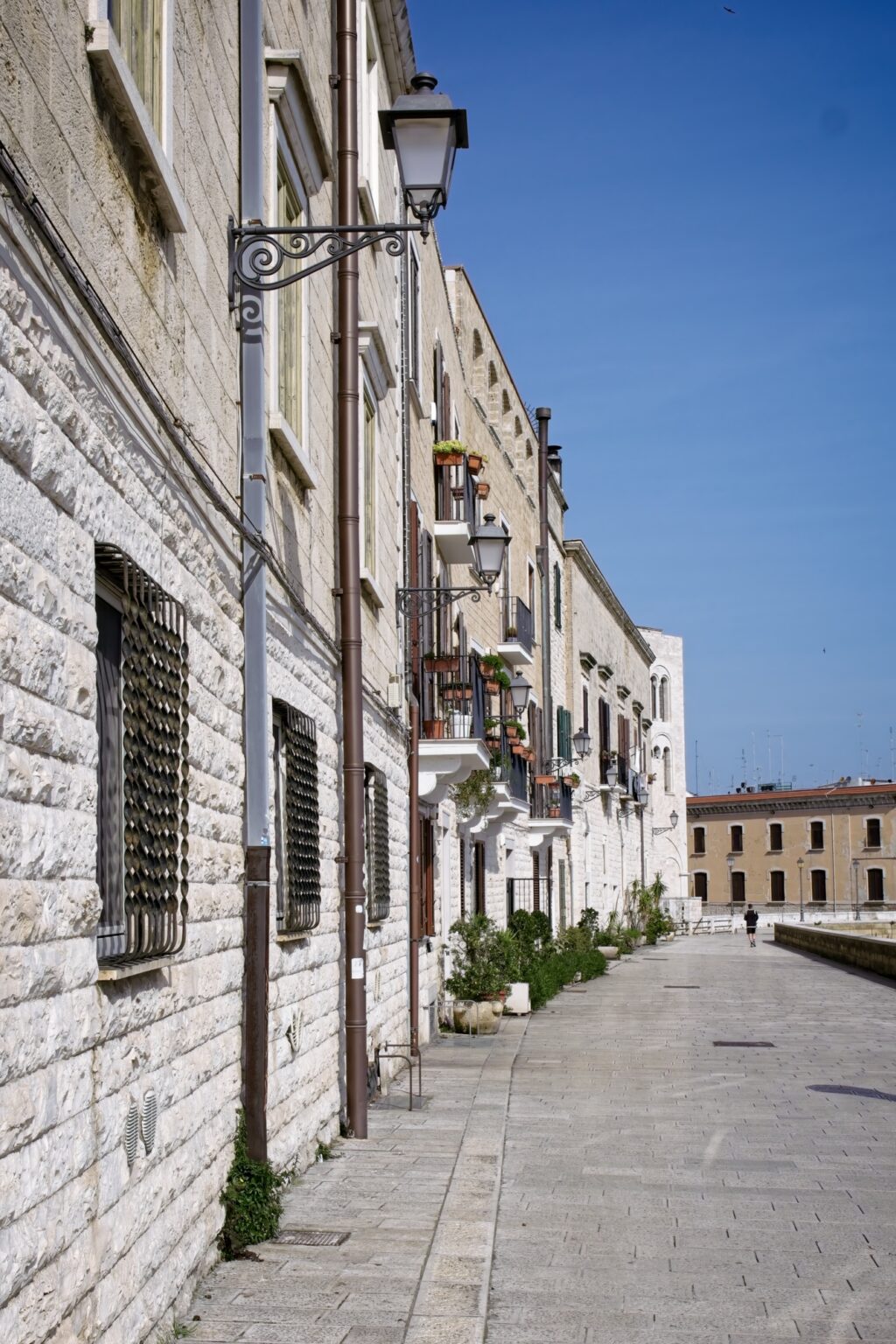 Minimalist street scene showing the clean stone architecture and long shadows of a quiet Bari side street