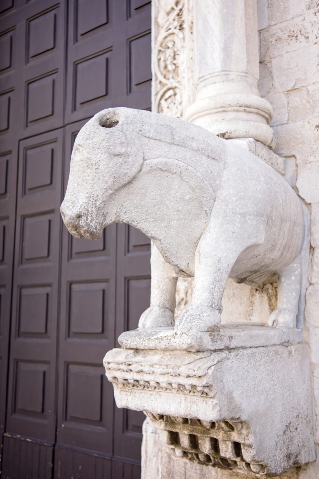 Close-up architectural detail of a weathered stone bull sculpture on a historic building in Bari