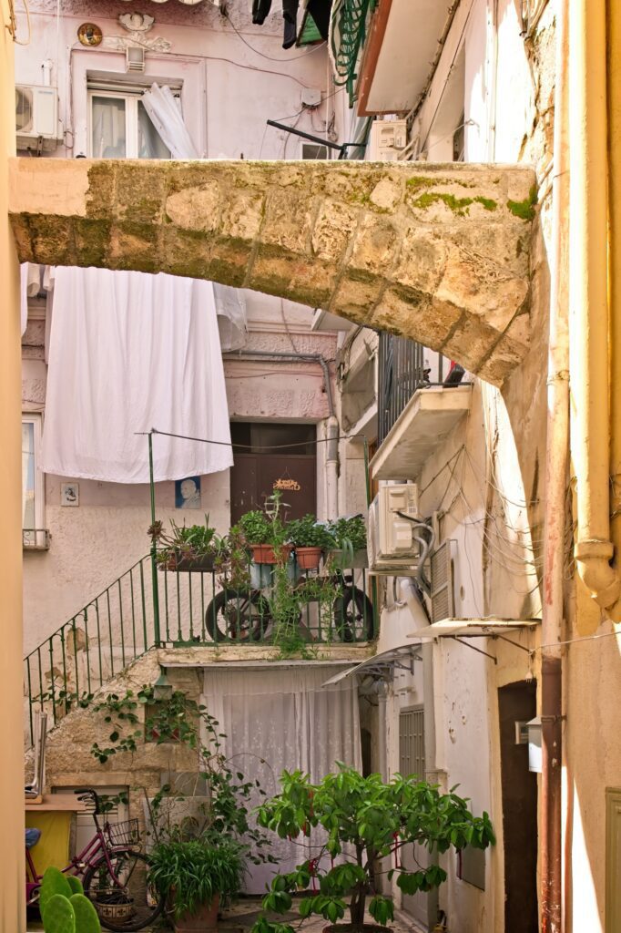 A candid, observational moment of laundry hanging in a sun-drenched arched alleyway in Bari, Italy