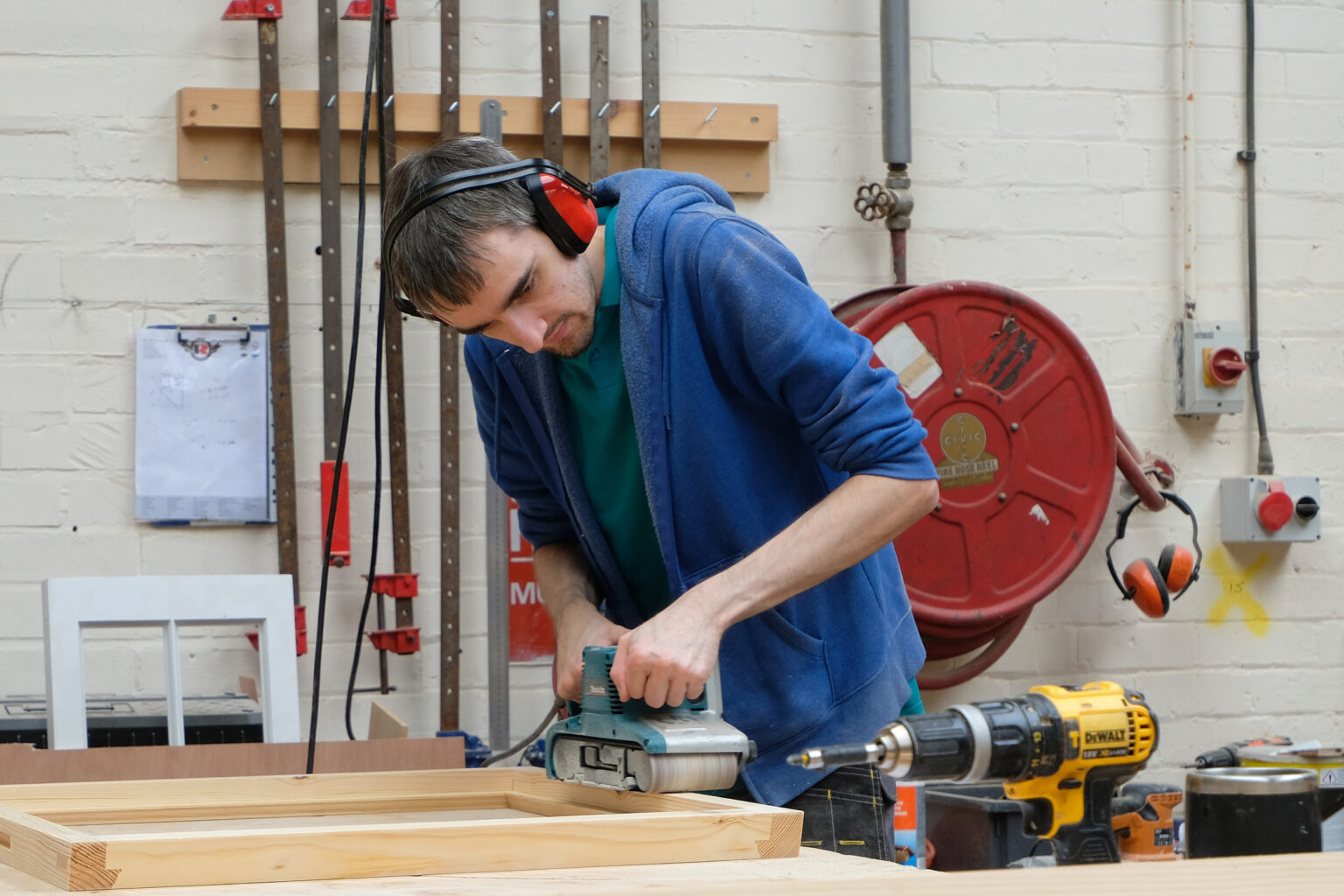 A craftsman using a handheld power planer on a timber edge at a workshop workbench.