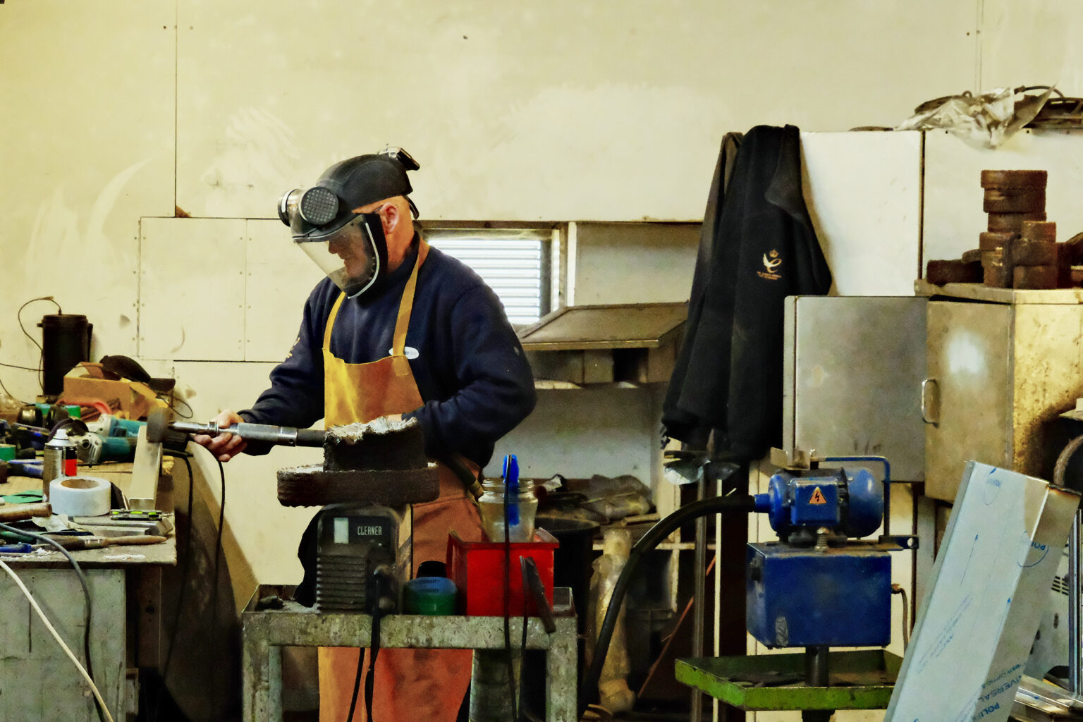 A manufacturing employee polishing metal components and wearing PPE equipment.