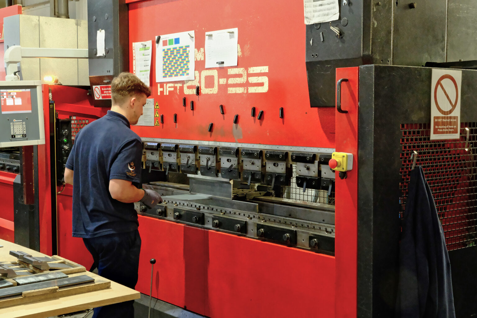 A worker operating a heavy industrial sheet metal bending press inside a factory setting.