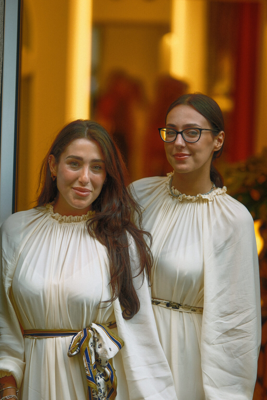 A candid portrait of two female colleagues wearing matching cream dresses in a softly lit boutique