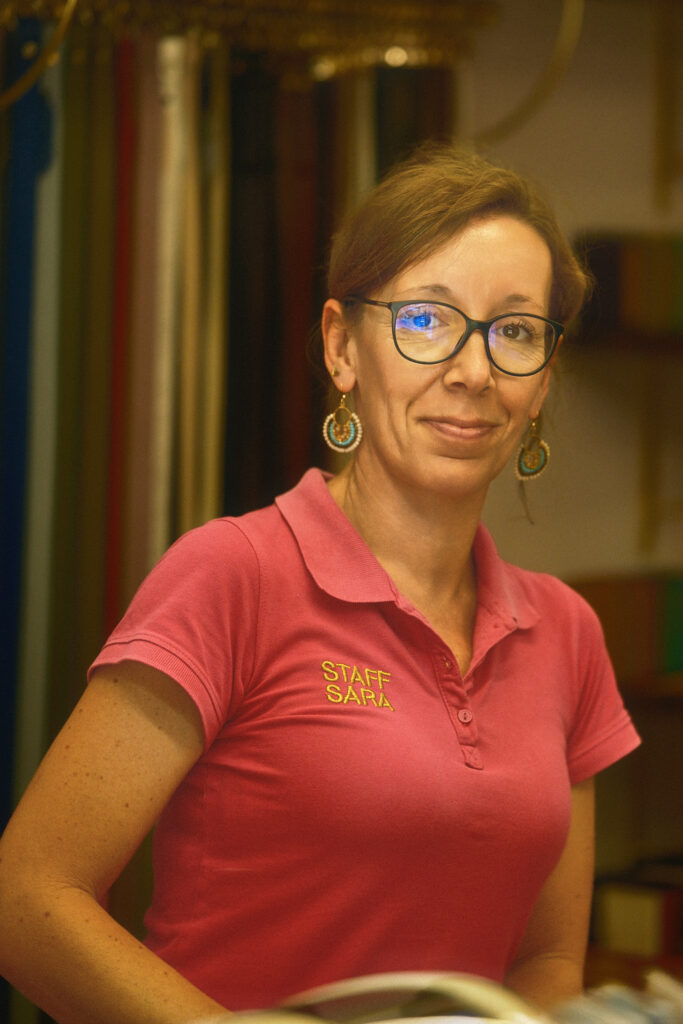 A documentary portrait of a female worker wearing glasses and a pink polo shirt in an authentic workplace environment.