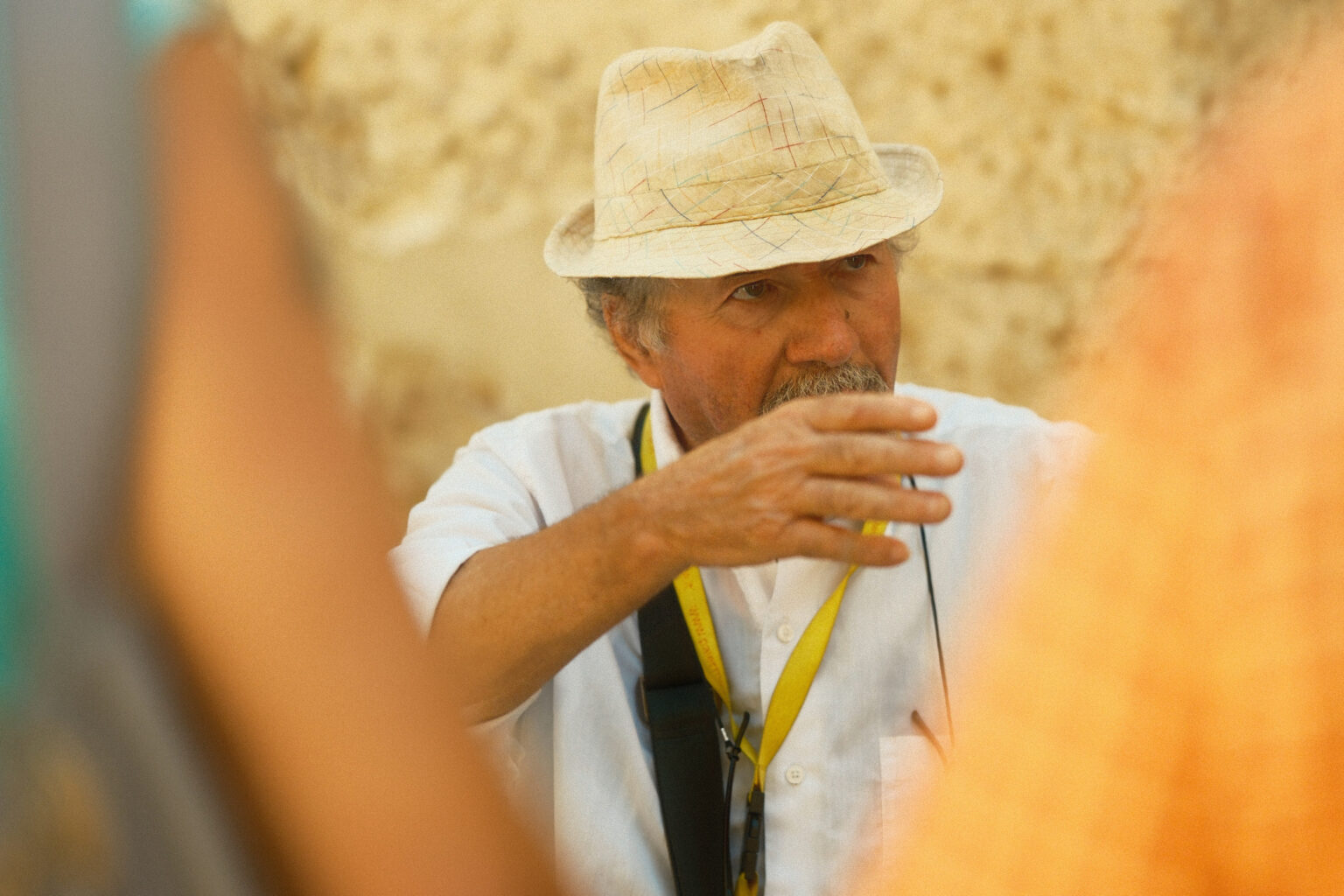 An editorial portrait of a tour guide in a straw hat gesturing mid-conversation, emphasizing natural lighting and candid storytelling.