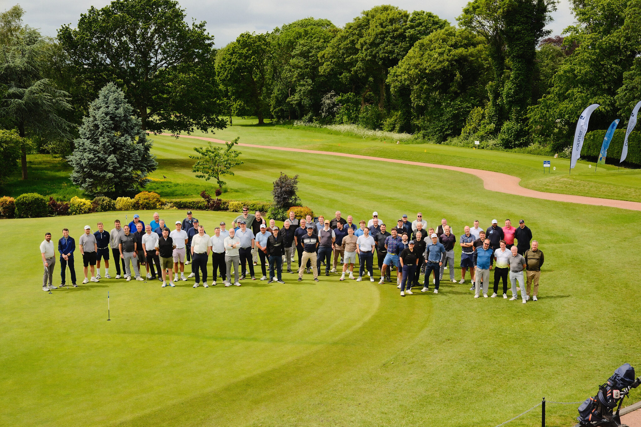 A wide corporate group portrait of all tournament attendees lined up across a golf green for a charity fundraising outcome photo.