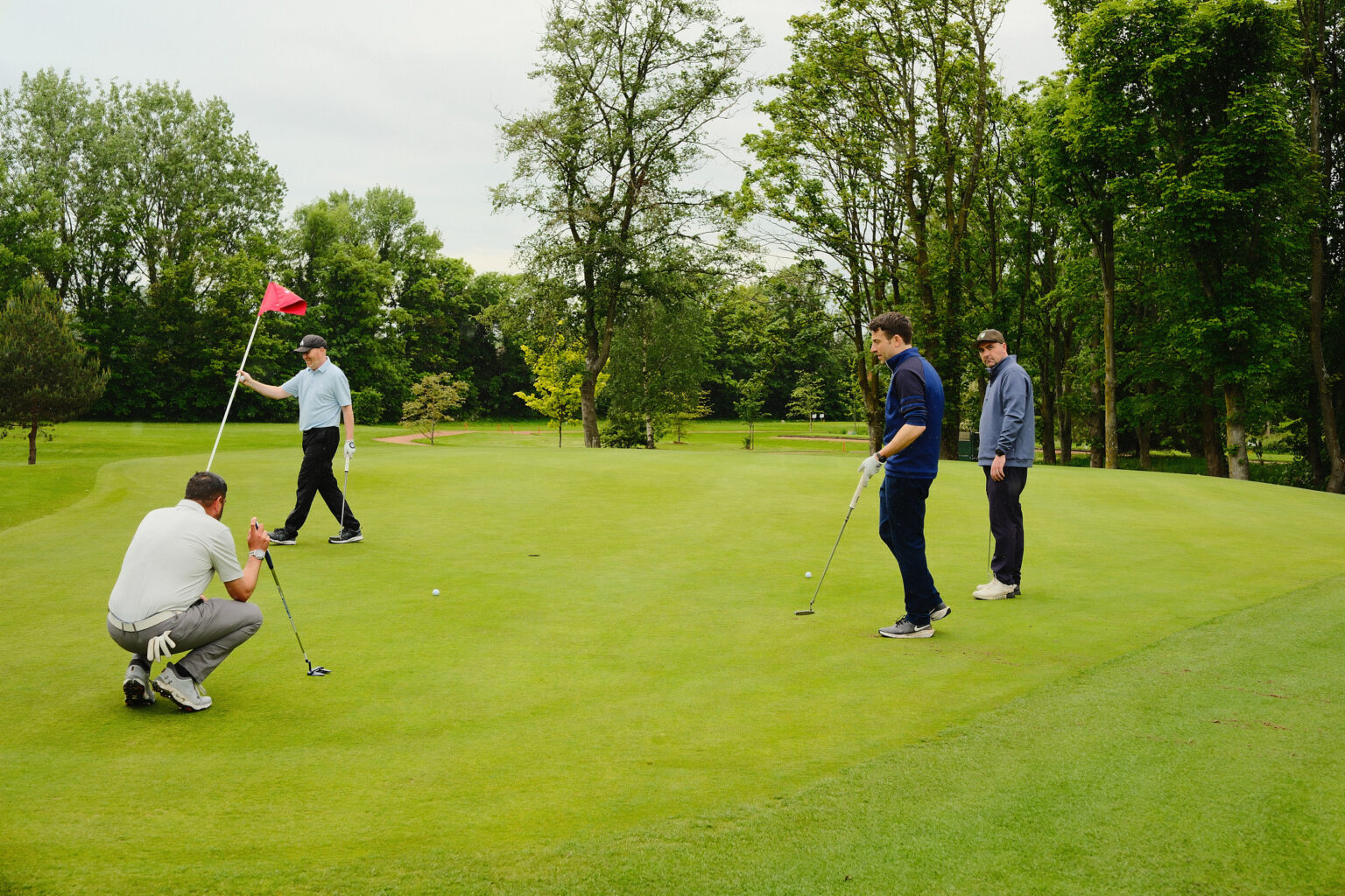 A low-angle close-up of participants checking a golf hole marker on the green during a branded charity match.