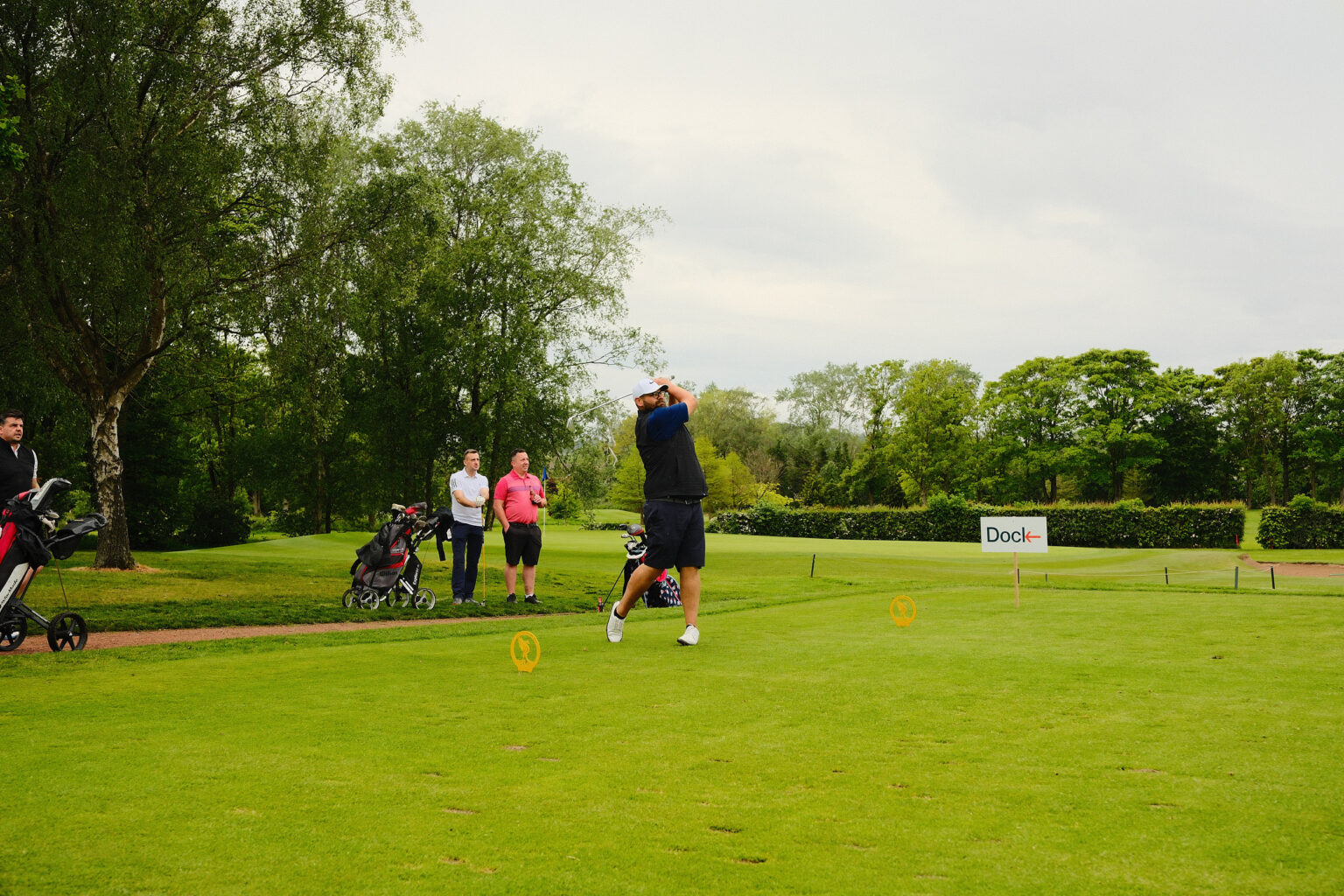 A mid-distance shot of a corporate client teeing off while his team watches on