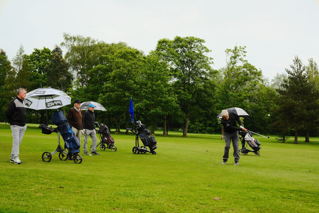 Participants using umbrellas on a golf course, showcasing candid documentary event photography under changing weather conditions.