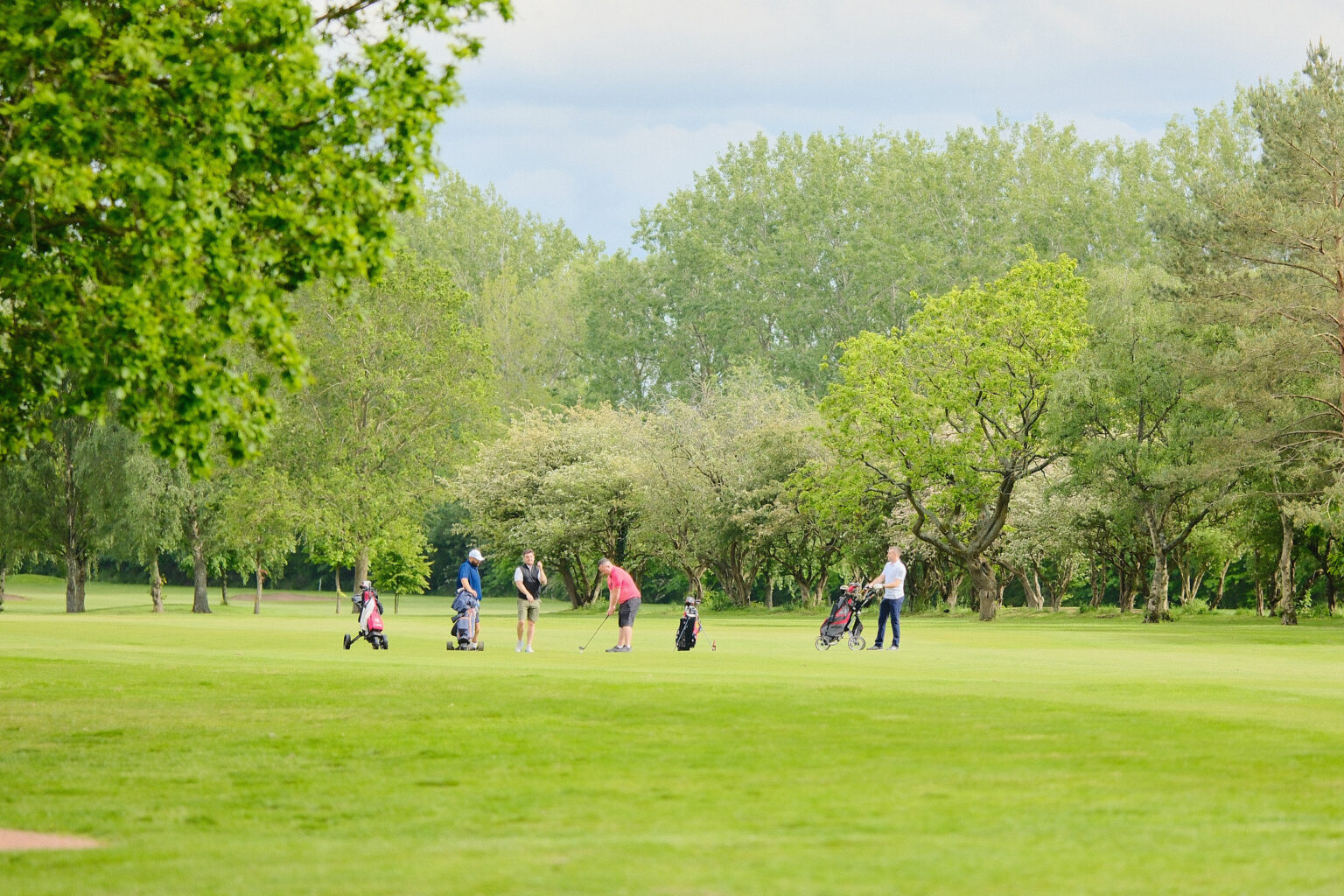 A wide-angle landscape shot showing multiple corporate event groups dispersed across an expansive green golf course.