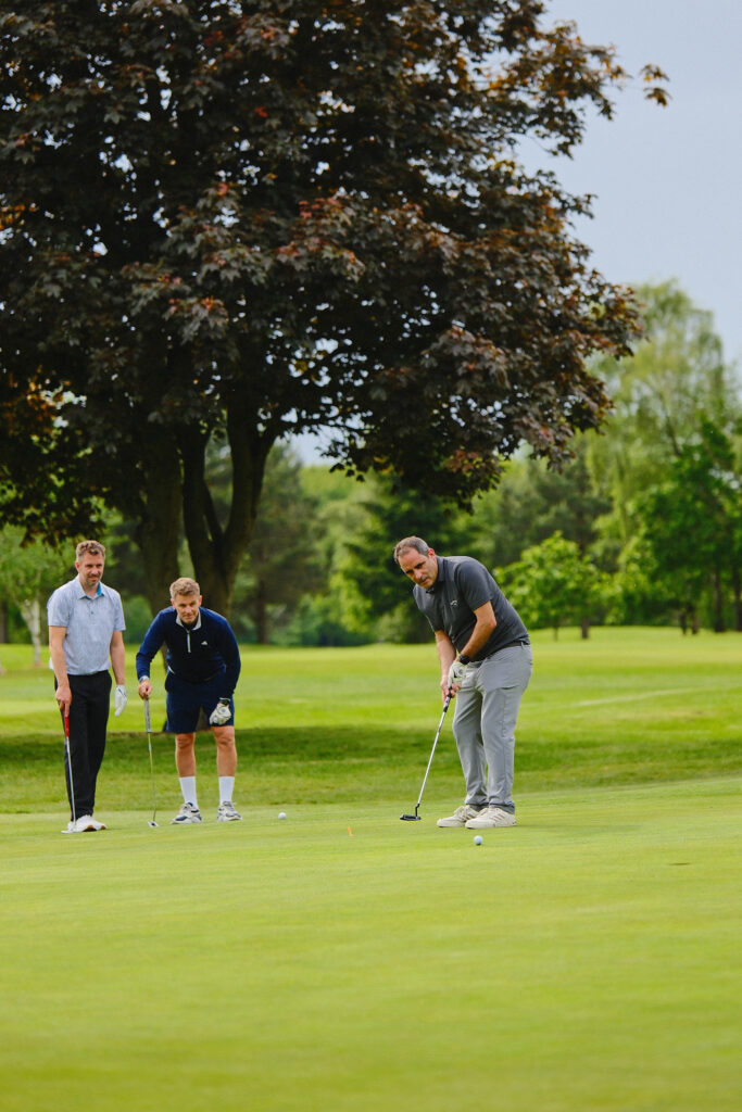 Two corporate event participants observing a third putting during a charity golf tournament.
