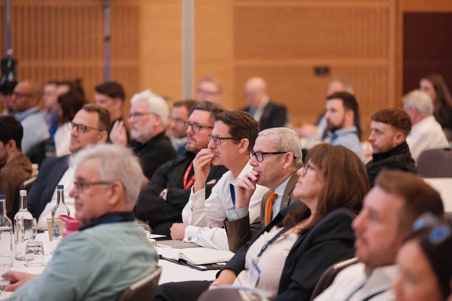 Rows of seated corporate delegates listening to a presentation inside a large conference theater hall.