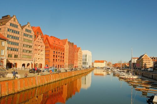 Wide shot of the Ołowianka Island waterfront showing the symmetry of modern gabled buildings reflected in the calm river water.