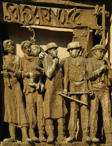 A bronze bas-relief sculpture titled "Solidarność" (Solidarity), depicting a group of shipyard workers, a woman, and a man holding a child, symbolizing the collective unity of the Polish labor movement.