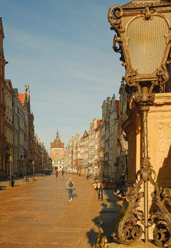 Perspective view looking down the Royal Route toward the Green Gate, featuring ornate historic street lamps and the weathered stone textures of the Old Town.